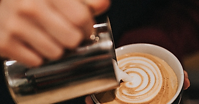 Barista gießt kunstvoll Milchschaum in Cappuccino und kreiert Latte-Art im Café in Hamburg
