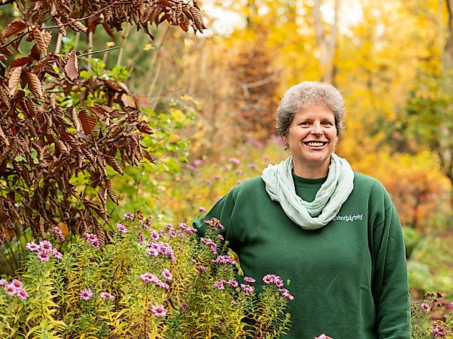 Lächelnde Person im herbstlich blühenden Garten in Hamburg, umgeben von buntem Laub und Wildstauden