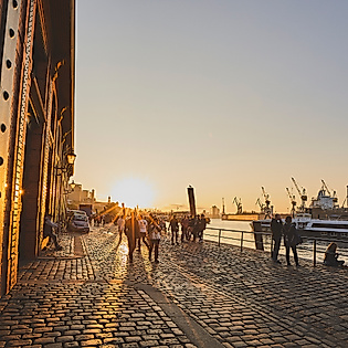 Sonnenaufgang am Hamburger Fischmarkt mit Lichtreflexen auf Backsteinfassade und Blick auf den Hafen