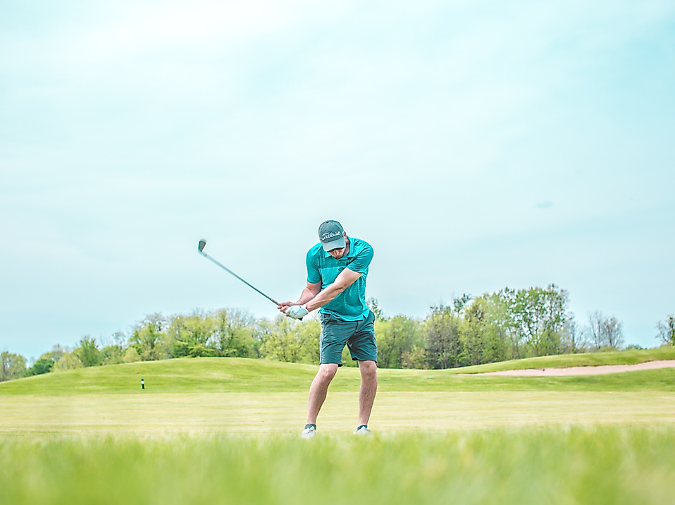 Golfer beim Abschwung auf sonnigem Fairway in der Golfregion Hamburg, umgeben von Natur