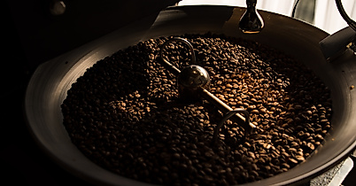 Frisch geröstete Kaffeebohnen in einer Rösttrommel, beleuchtet durch warmes Licht.