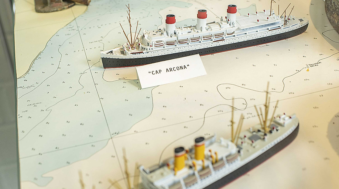 Auf einer Seekarte sind zwei Schiffe abgebildet, darunter das Passagierschiff Cap Arcona. Der Name Cap Arcona steht stellvertretend für die Ereignisse am 3. Mai 1945.