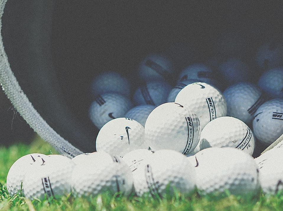 Mehrere Golfbälle rollen aus einem Eimer auf eine Rasenfläche – Symbolbild für Golfangebote in Hamburg