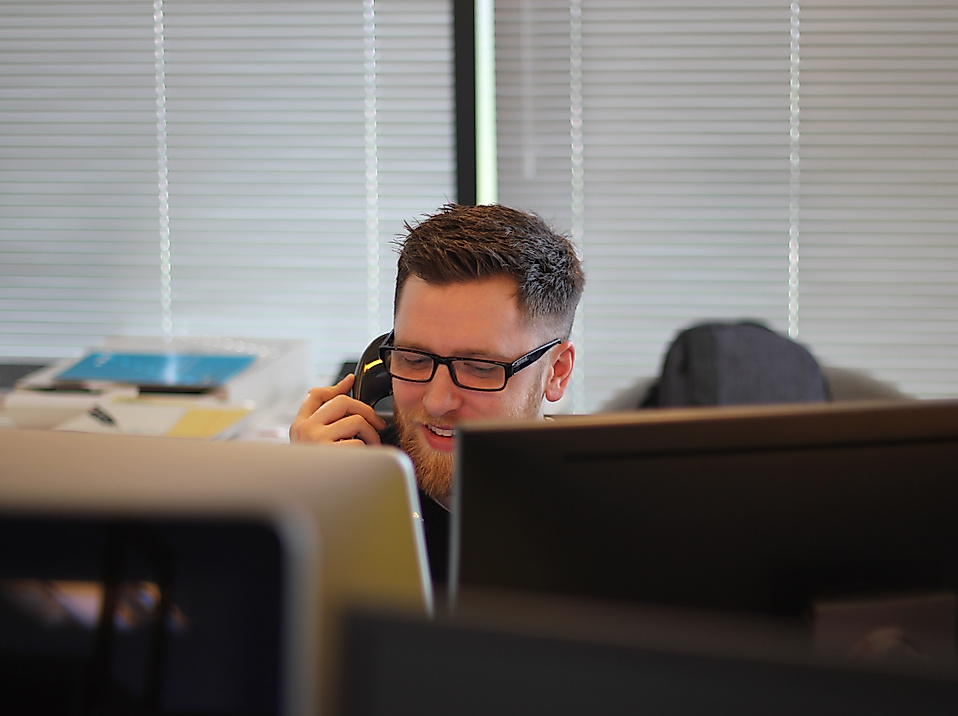 Mitarbeiter im Service Center telefoniert am Schreibtisch zwischen Monitoren und Unterlagen