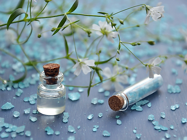 Kleine Glasfläschchen mit Badezusatz und blauen Kristallen auf dekorativer Wellness-Oberfläche