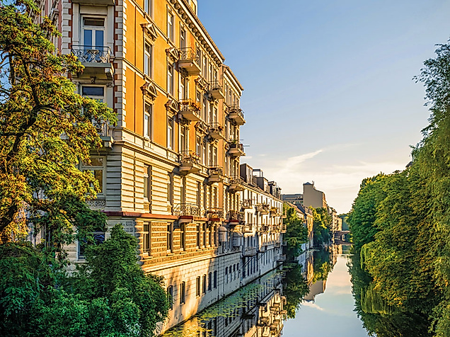 Jugendstilfassaden am Alsterkanal in Hamburg bei Sonnenuntergang, gesäumt von Bäumen und Wasserreflexionen