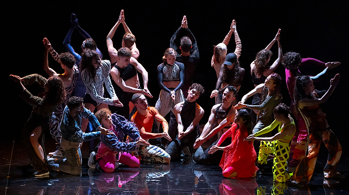 Ausschnitt aus Marco da Silva Ferreiras »A Folia«. Eine Gruppe Tänzer*innen steht in einem Halbkreis mit bunten Kostümen.