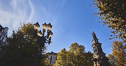Laterne und St.-Georg-Brunnen auf dem Hansaplatz in Hamburg bei blauem Himmel und herbstlich belaubten Bäumen
