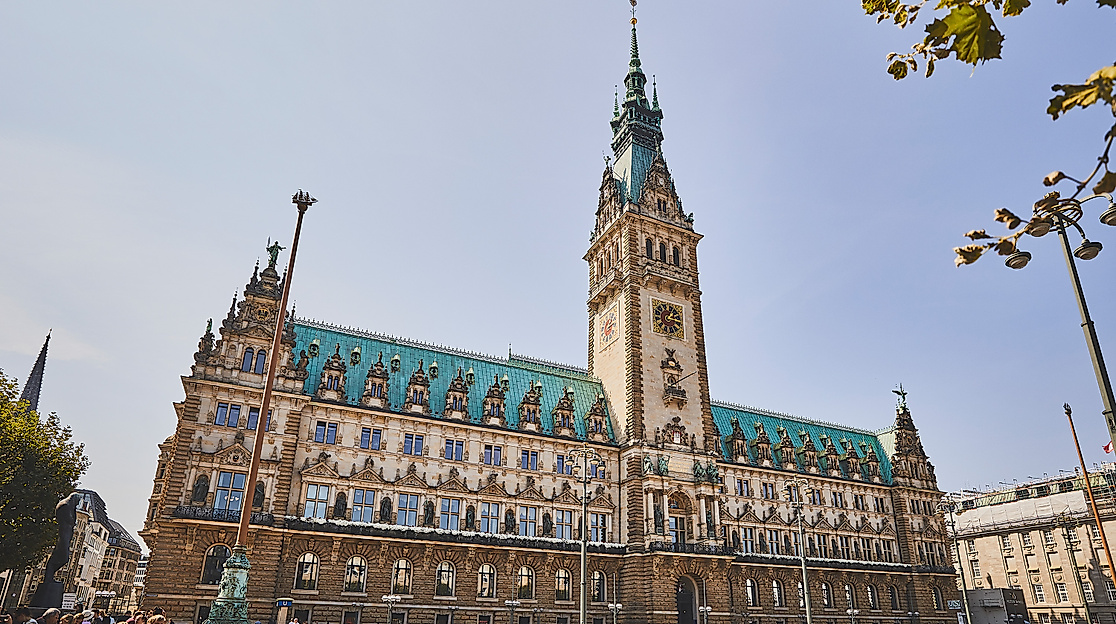 Hamburger Rathaus bei Sonnenschein mit Blick auf den belebten Rathausmarkt