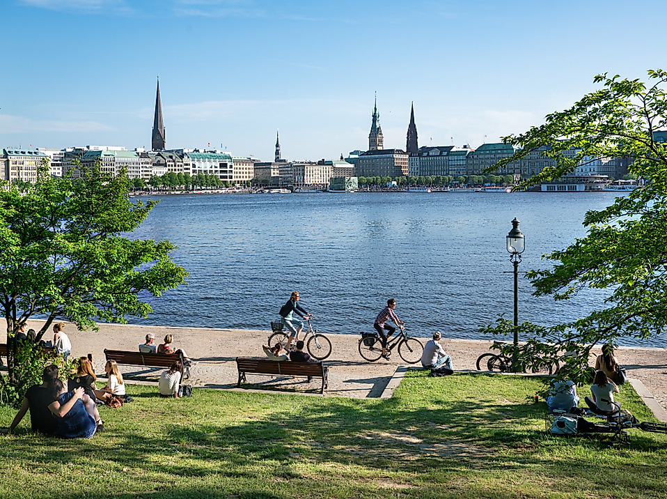 Menschen entspannen und radeln im Sommer an der Binnenalster mit Blick auf Hamburgs Skyline