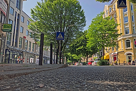 Grüne Bäume säumen die Gertigstraße in Hamburg, umgeben von Altbauten, Cafés und kleinen Geschäften