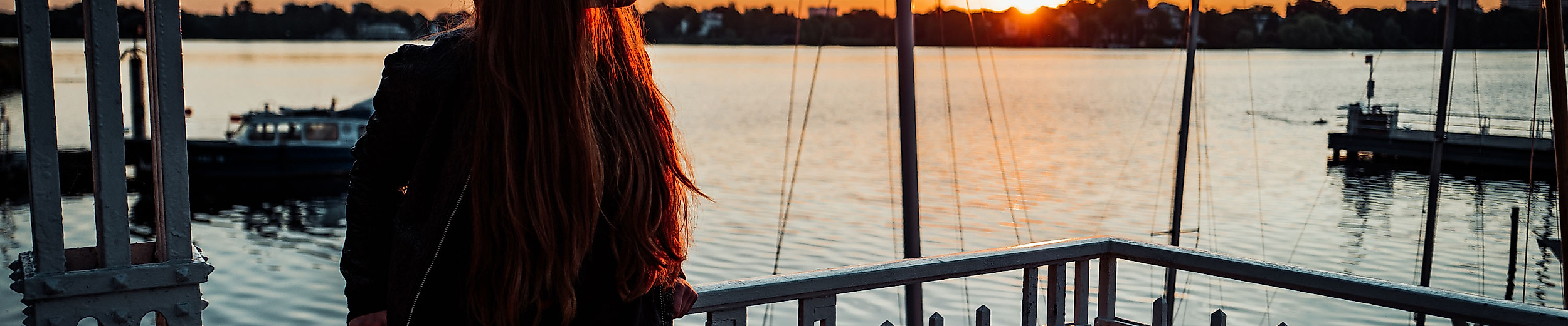 Person steht bei Sonnenuntergang auf einem Bootssteg an der Außenalster mit Blick auf das Wasser