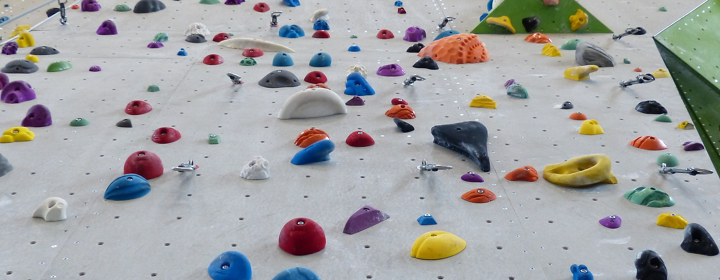 Hohe Indoor-Kletterwand mit bunten Griffen und Sicherungsseilen für verschiedene Schwierigkeitsgrade