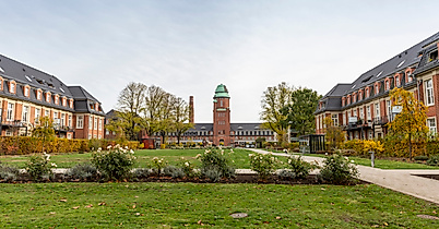Symmetrischer Innenhof mit Rasen und Blumen in Hamburg-Dulsberg, im Hintergrund Backsteinbauten mit Uhrenturm.