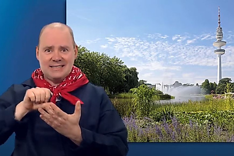 Mann gebärdet vor Hamburg-Kulisse mit Parklandschaft und Fernsehturm – barrierefreie Infos zu Grünflächen.