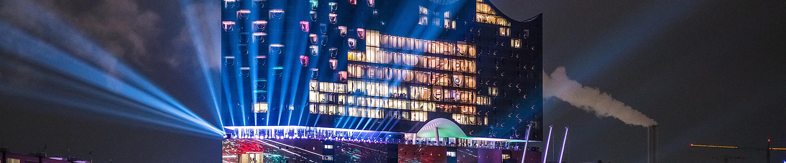 Illuminierte Elbphilharmonie bei Nacht mit bunter Lichtshow und Spiegelungen auf der Elbe