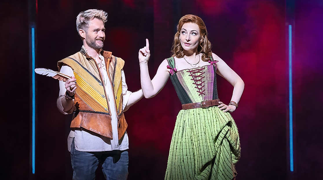 Szenenbild & Julia: William Shakespeare mit Schreibfeder und Anne Hathaway, die mit dem Finger aufzeigt. 