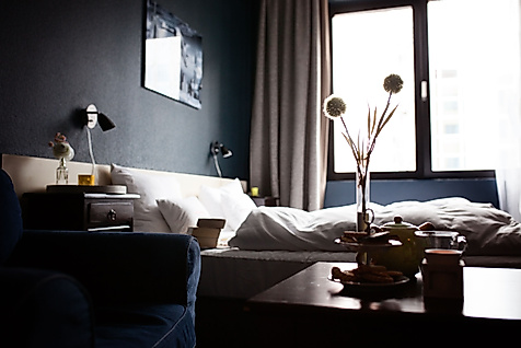 Gemütlich eingerichtetes Schlafzimmer mit Doppelbett, dunklen Wänden und Tageslicht durch ein großes Fenster.