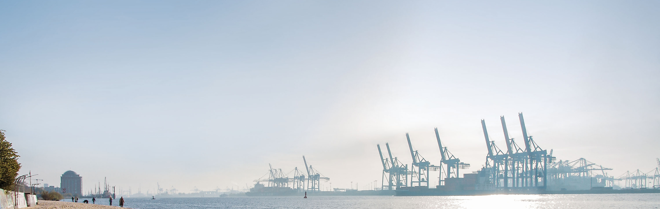 Sonniger Elbstrand mit Blick auf Containerkräne im Hamburger Hafen und glitzerndem Wasser