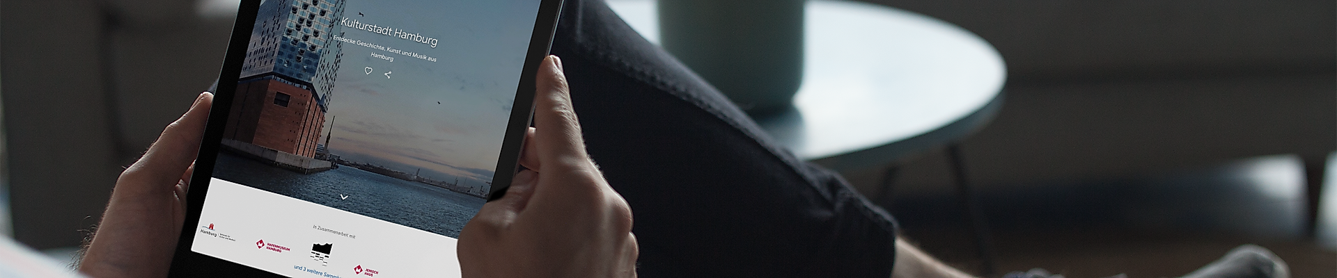 Person nutzt ein Tablet auf dem Sofa, digitale Kulturangebote bequem von zuhause