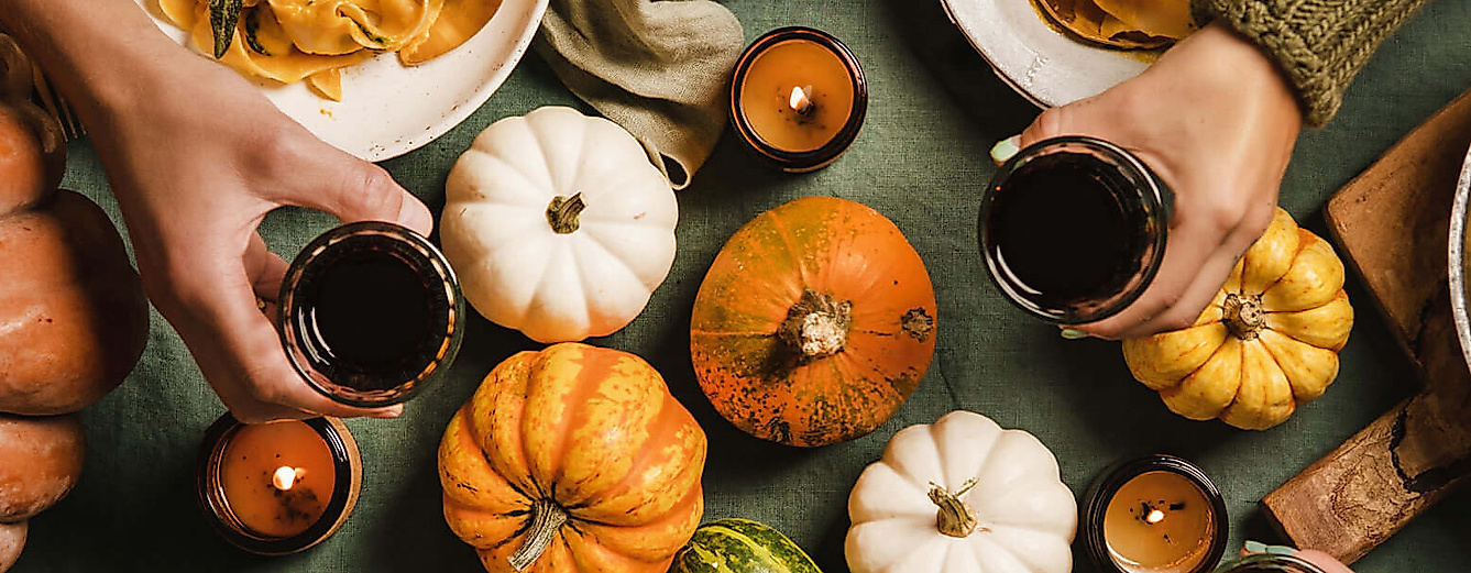 mit Rotwein anstoßende Hände über einem herbstlich gedeckten Tisch