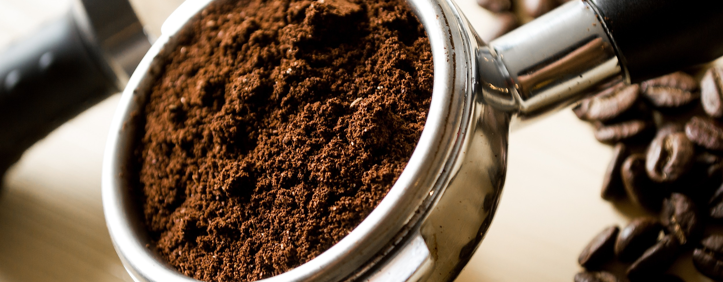 Frisch gemahlener Kaffee im Siebträger, umgeben von gerösteten Bohnen auf hellem Untergrund