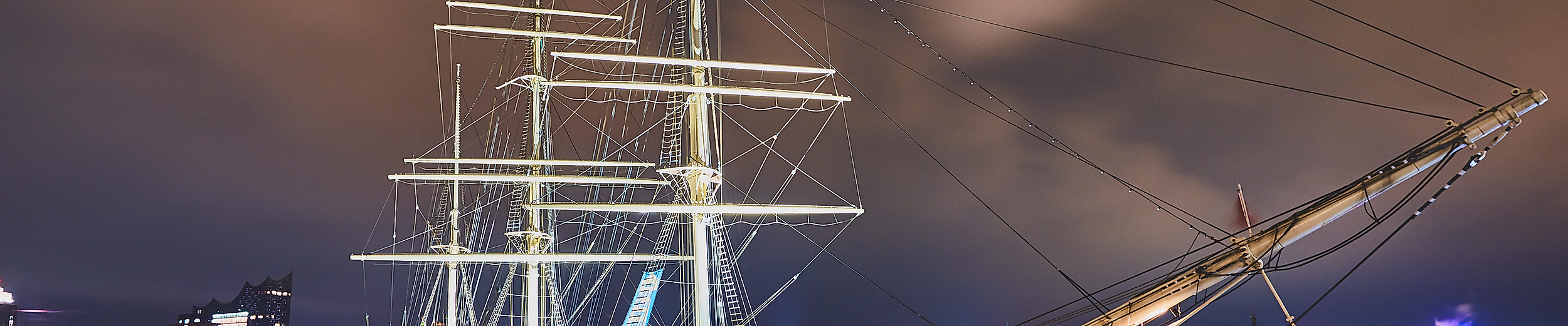 Das beleuchtete Museumsschiff Rickmer Rickmers liegt nachts im Hamburger Hafen vor illuminiertem Himmel
