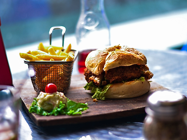 Frischer Burger mit Pommes auf Holzbrett, serviert in Hamburger Restaurantambiente
