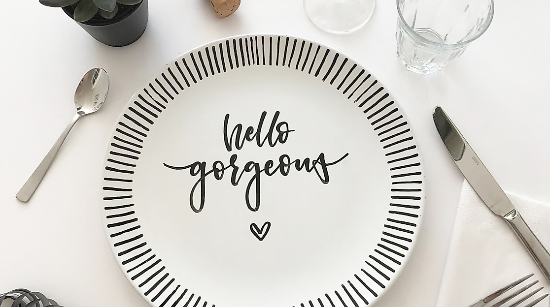 Teller mit Lettering „hello gorgeous“ auf kreativ gedecktem Tisch mit Besteck, Gläsern und Sukkulente