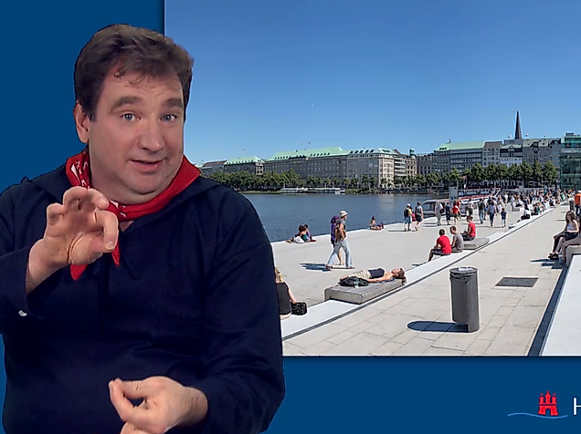 Man signing in International Sign in front of the Alster lake promenade in Hamburg on a sunny day.