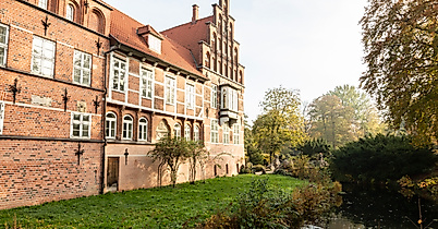 Backsteinfassade des Bergedorfer Schlosses in Hamburg mit Wassergraben und Bäumen im Sonnenlicht.