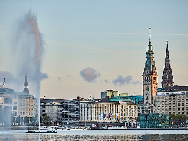 Blick über die Binnenalster auf das Hamburger Rathaus und die Alsterfontäne bei Abendlicht