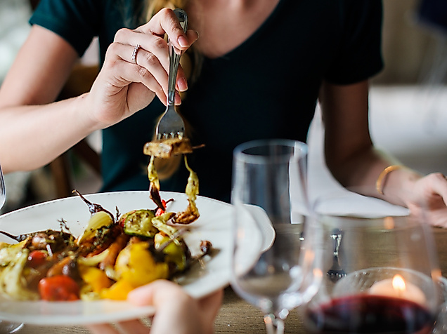 Person genießt buntes Gemüsegericht bei Kerzenschein und Rotwein in stilvollem Restaurant
