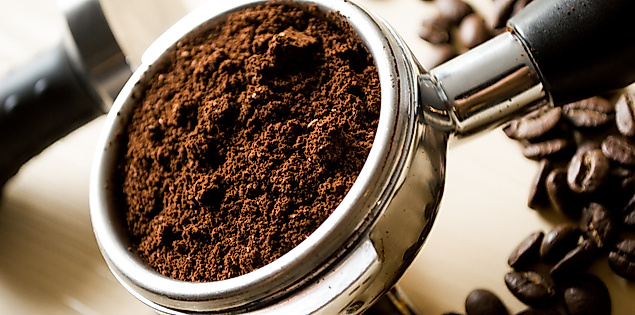 Frisch gemahlener Kaffee im Siebträger, umgeben von gerösteten Bohnen auf hellem Untergrund