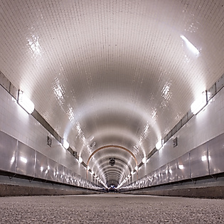 Symmetrischer Blick durch den beleuchteten Alten Elbtunnel mit gekachelten Wänden und gewölbter Decke
