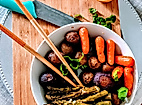 Bunte vegane Bowl mit Gemüse, Falafel und Sesam, serviert auf Holzbrett mit Essstäbchen und Zitrone