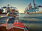 Junger Mann auf einer Barkasse im Hamburger Hafen mit Elbkränen im Hintergrund