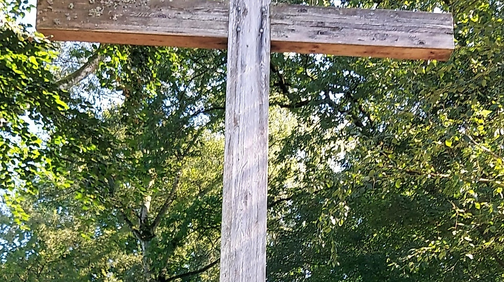 Holzkreuz, dahinter Bäume