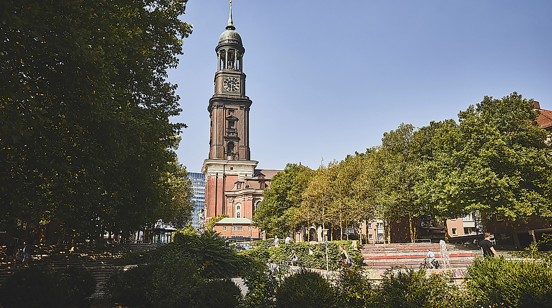 Turm der Hauptkirche St. Michaelis hinter Bäumen vor blauem Himmel in Hamburg.