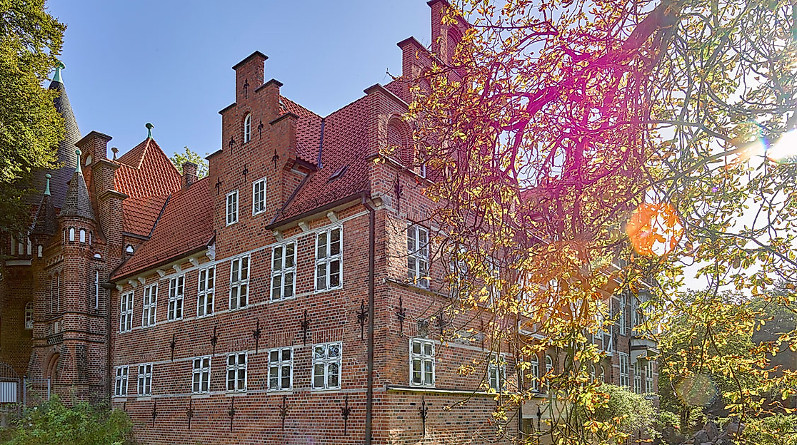 Bergedorfer Schloss mit rotem Ziegeldach und Giebeln, teils verdeckt von herbstlich leuchtenden Baumkronen