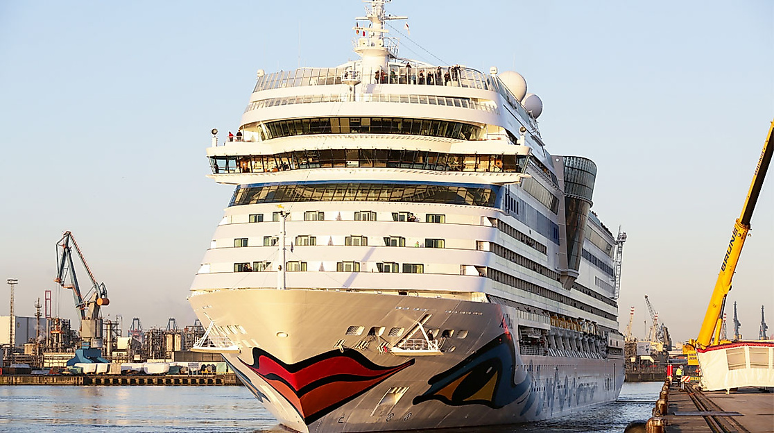 AIDAsol liegt am Kai im Hamburger Hafen, im Hintergrund Kräne und Hafenanlagen bei Abendlicht
