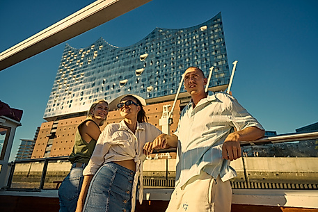 Drei Menschen auf einem Boot vor der Elbphilharmonie.