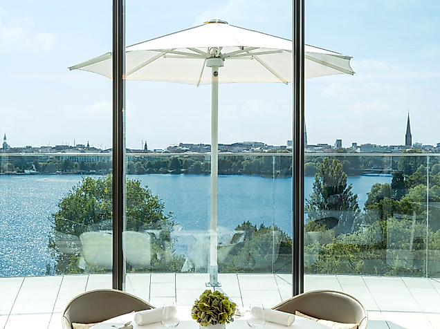 Elegant gedeckter Tisch im The Fontenay mit Panoramablick auf die Alster und weiße Sonnenschirme.