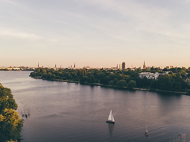 Luftaufnahme der Außenalster mit Segelbooten und Blick auf Hamburgs Skyline im Abendlicht.