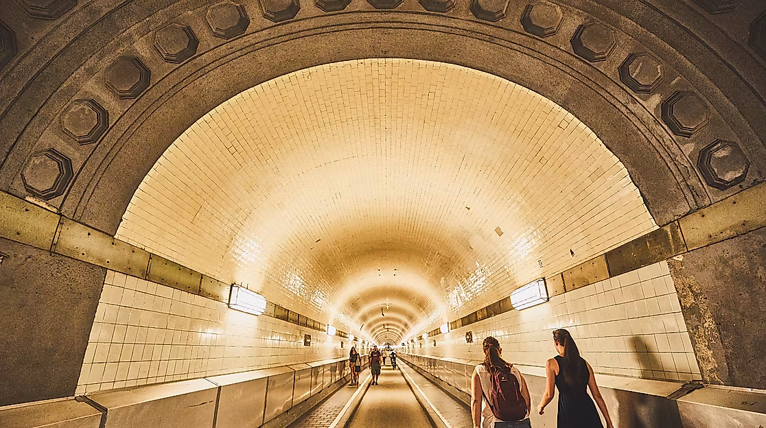 Fußgänger:innen im beleuchteten Tunnelgewölbe des historischen Alten Elbtunnels in Hamburg