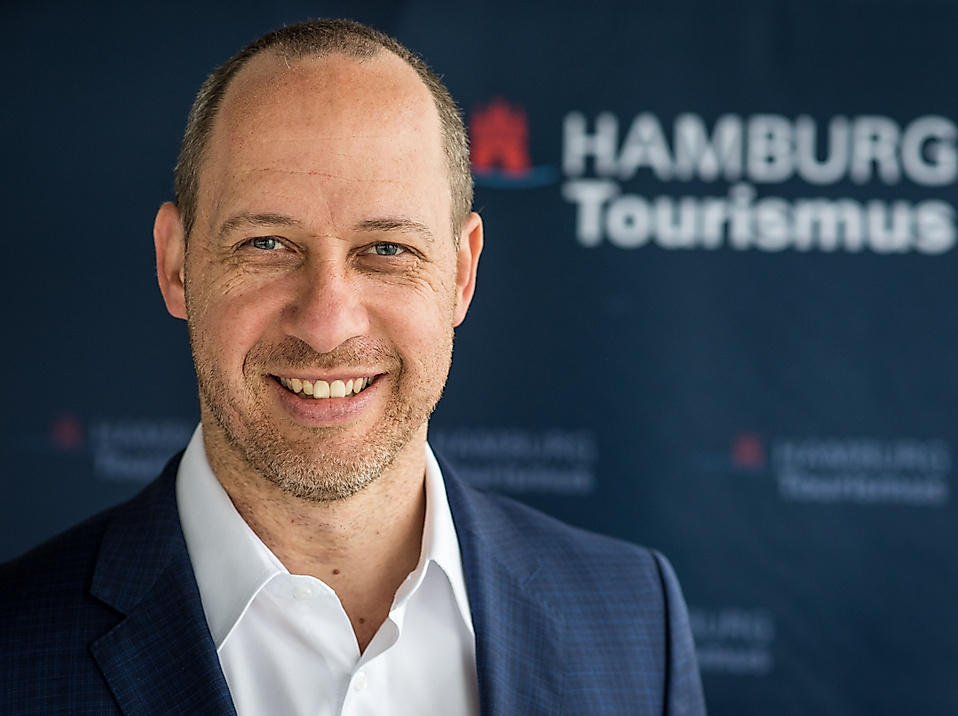 Michael Otremba, Geschäftsführer der Hamburg Tourismus GmbH, vor blauem Hintergrund mit HHT-Logo.