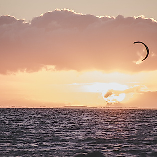 Windsurfer vor Sonnenuntergang auf dem Meer unter wolkenverhangenem Himmel