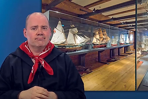 Mann gebärdet vor Ausstellungsraum mit maritimen Objekten – barrierefreie Infos zu Kultur in Hamburg.