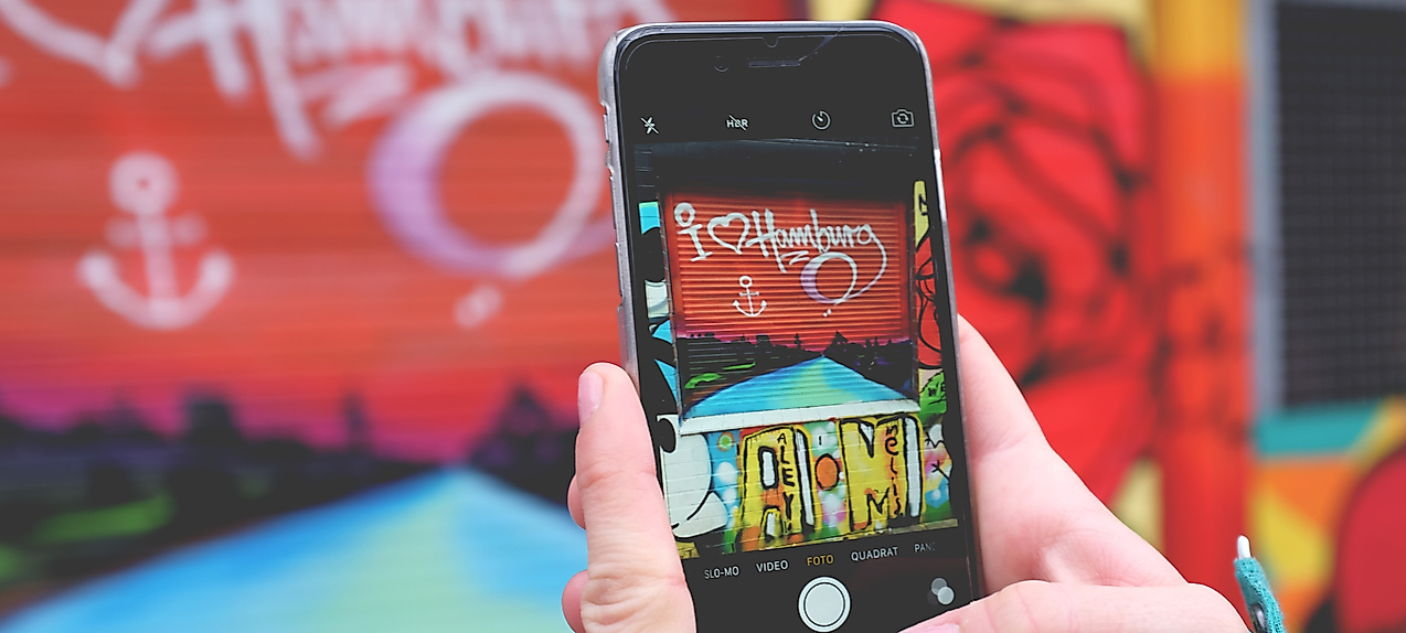 Smartphone fotografiert buntes Hamburg-Graffiti, Symbol für Social Media und Influencer-Kommunikation