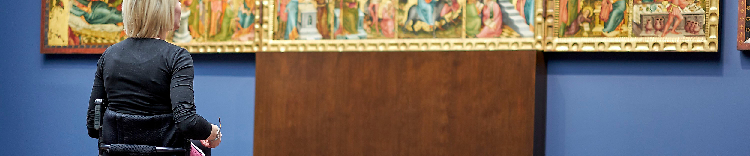 Rollstuhlfahrerin betrachtet ein mehrteiliges historisches Gemälde in der barrierefreien Hamburger Kunsthalle.